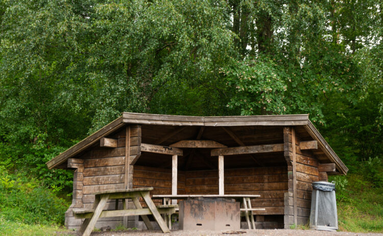 Ett vindskydd på Flottbro friluftsområde mot en grönskande bakgrund av skog.