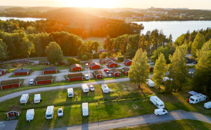 Camping i Stockholm vid sjö och natur–Vy av campingplats med husvagnar och stugor i solnedgången omgiven av skog, i bakgrunden syns en sjö.