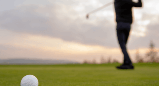 närbild på golfboll med en spelare i siluett på en green.