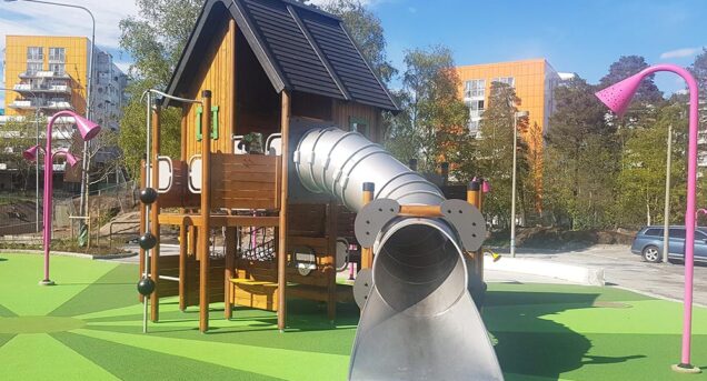 bild på Flemmingsbergsparken i Huddinge, en lfärgglad lekställning och grönt gräs mot blå himmel.